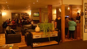 A hotel lobby with leather sofas, a wooden coffee table, and a TV screen. - Pedlars Motel (Paeroa)
