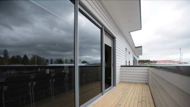 A balcony with a wooden floor and glass doors leading to a covered outdoor area. - Pedlars Motel (Paeroa)