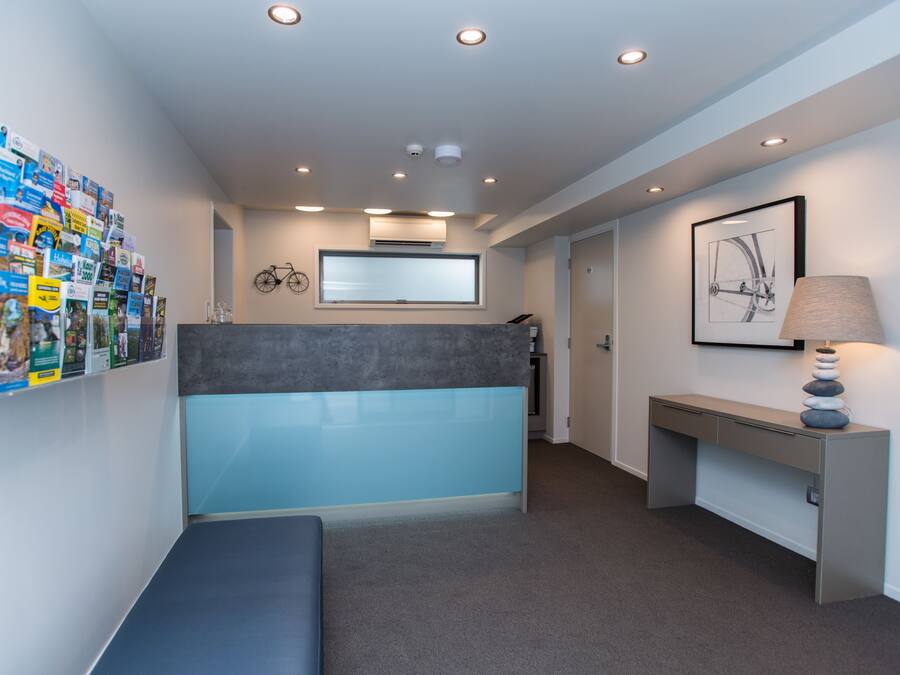 A reception area with a blue counter, a wall-mounted bicycle, a framed picture, and a desk with a lamp.