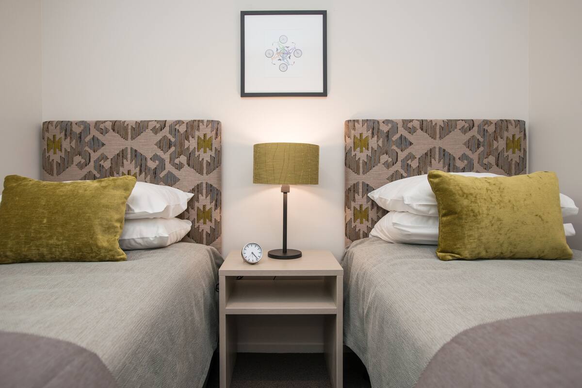 A twin room with two beds, each with a patterned headboard, a bedside table with a lamp, and a clock.