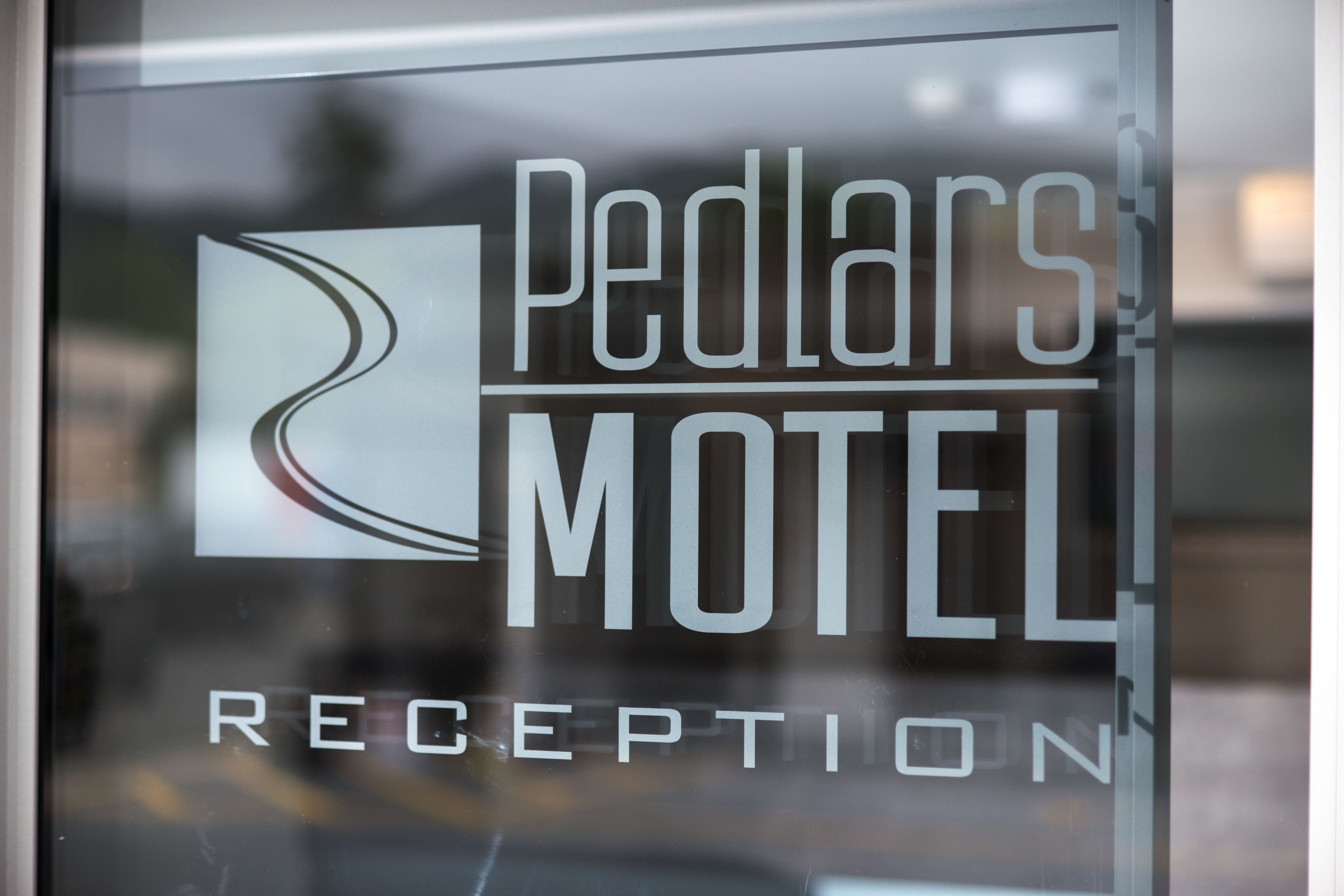 Zona de recepción con puerta de vidrio que muestra el texto "Pedlar's Motel" y "RECEPTION".