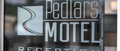 Zona de recepción con puerta de vidrio que muestra el texto "Pedlar's Motel" y "RECEPTION".