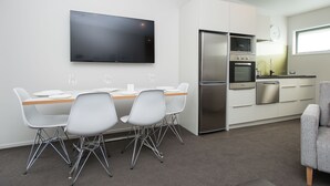 A modern kitchen with white cabinets, stainless steel appliances, and a flat-screen TV mounted on the wall. - Pedlars Motel (Paeroa)