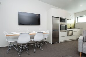 A modern kitchen with white cabinets, stainless steel appliances, and a flat-screen TV mounted on the wall. - Pedlars Motel (Paeroa)