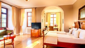 Une chambre d’hôtel avec un plancher en bois, un lit, une télévision, un canapé et un bureau avec une lampe.