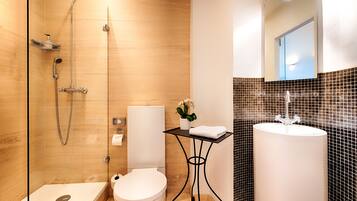 Un baño moderno con ducha de vidrio, inodoro blanco, lavamanos con salpicadero de azulejos negros y una pequeña mesa con planta en maceta.