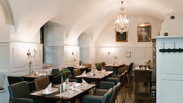 Un comedor formal con mesas dispuestas para el servicio, elegantes candelabros y decoración de pared clásica.