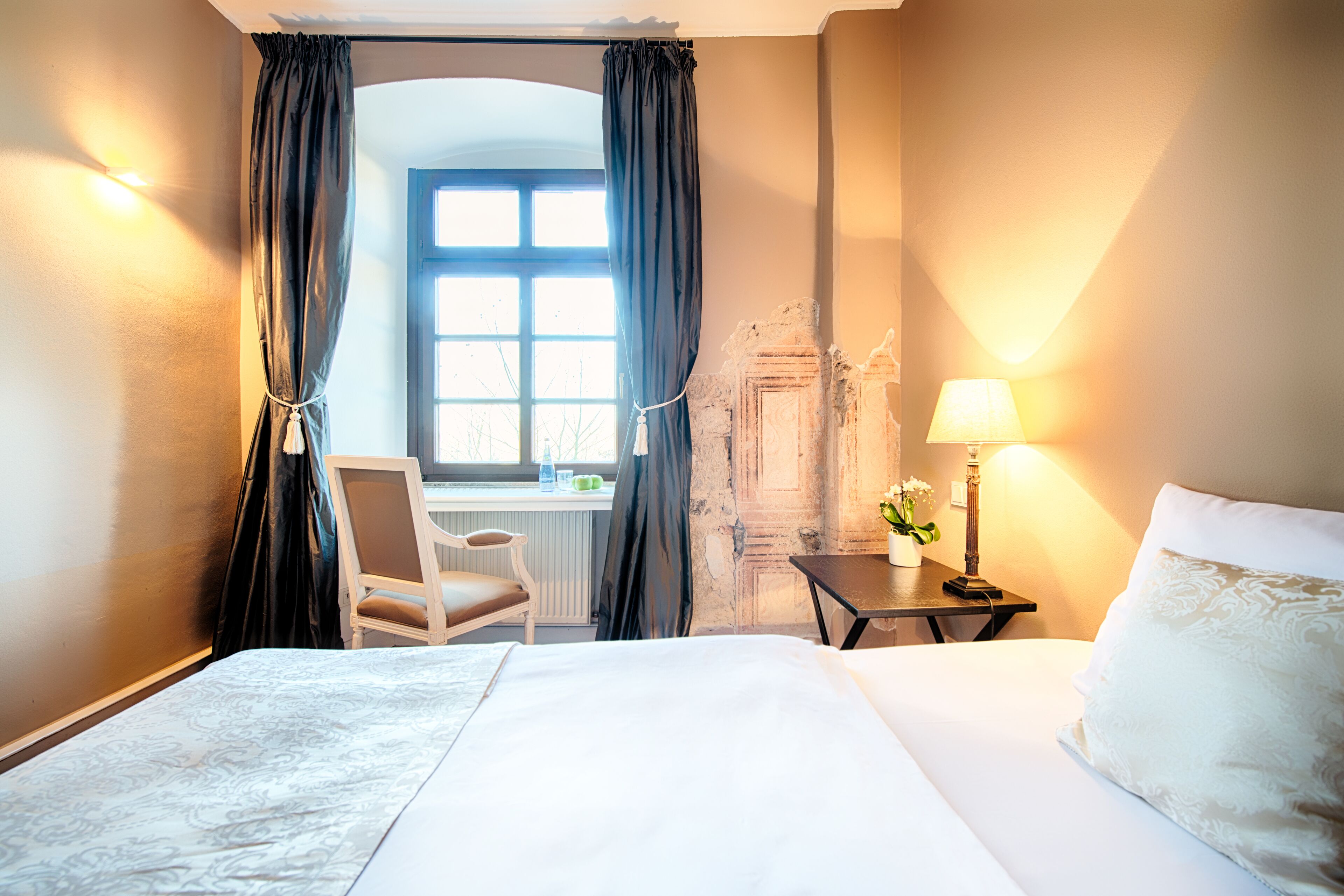 A hotel room with a bed, a desk, a chair, a lamp, and a view of the outdoors.