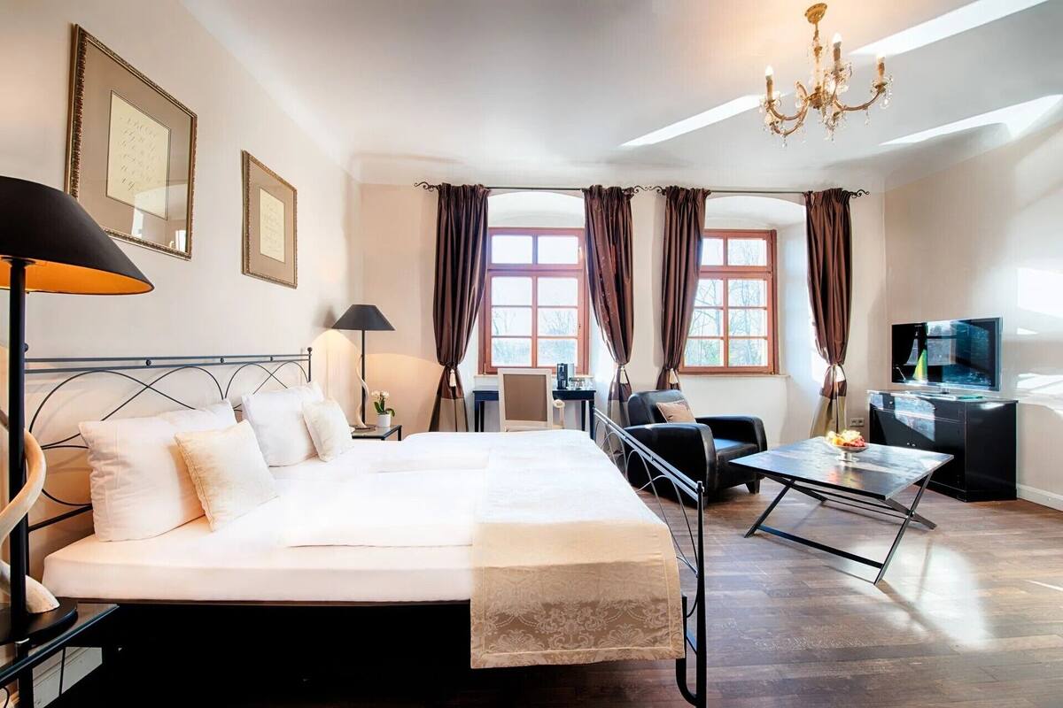 Una habitació d'hotel amb llit, escriptori, cadira, televisió i un lampadari.