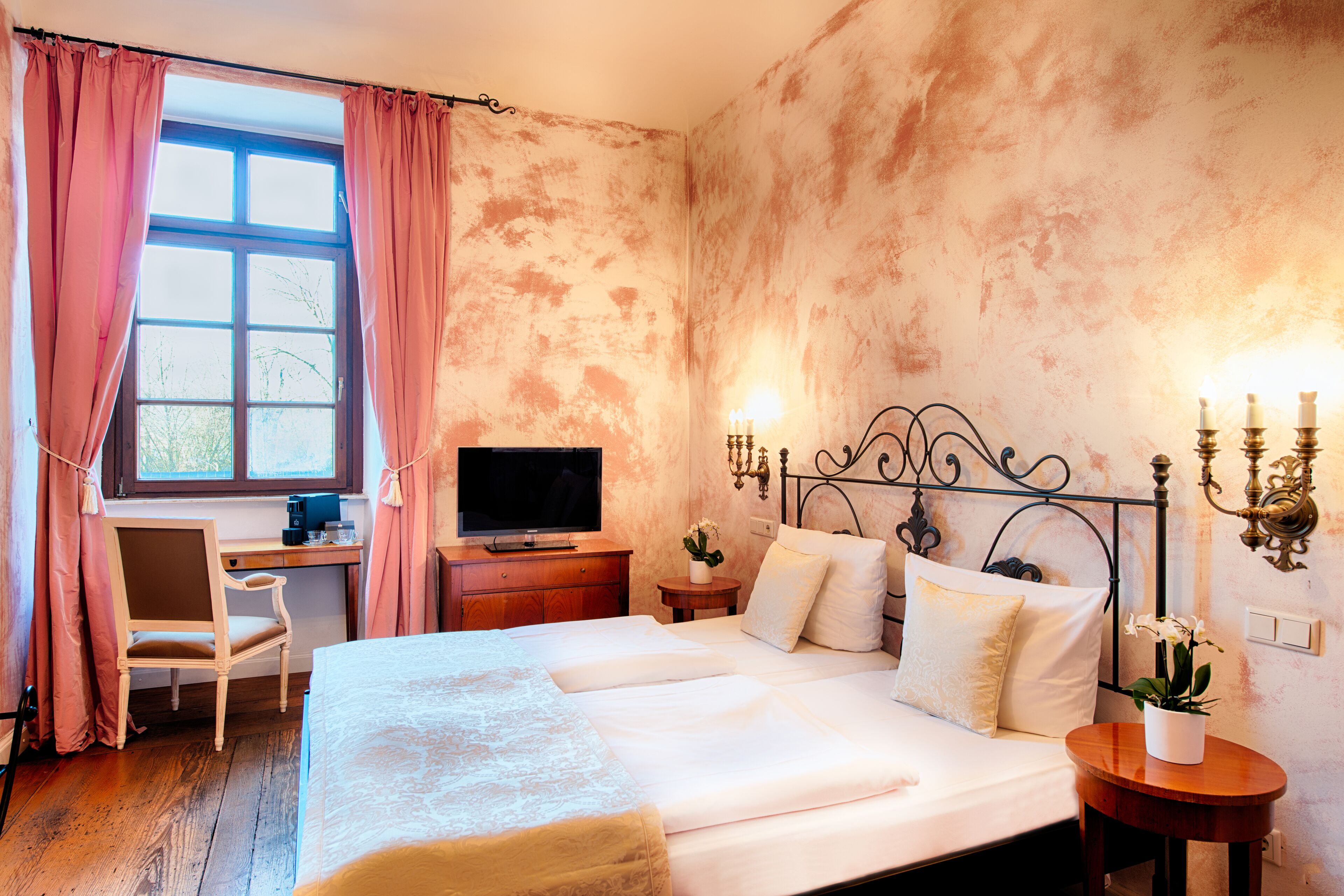 A bedroom with a bed, a desk, a television, and a wall-mounted light fixture.