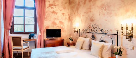 A bedroom with a bed, a desk, a television, and a wall-mounted light fixture.