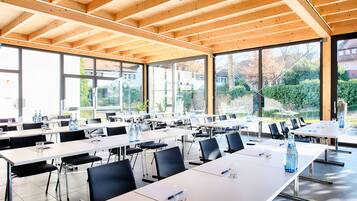 Een vergaderruimte met meerdere tafels en stoelen, grote ramen en een houten plafond.