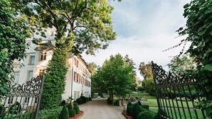A paved pathway leading to a building with a wrought iron gate, surrounded by well-maintained hedges and trees. - Hotel Schloss Lehen (Bad Friedrichshall)