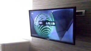 A flat-screen TV mounted on a textured wall in a room with a white radiator. - Pho Place (Bangkok)