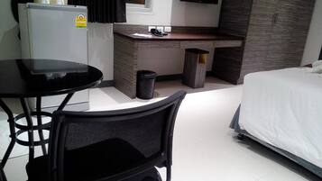 Ein Hotelzimmer mit einem Bett, einem Schreibtisch, einem Sessel, einem kleinen Tisch, einer Mülltonne, einem Kühlschrank und einem Fernseher.
