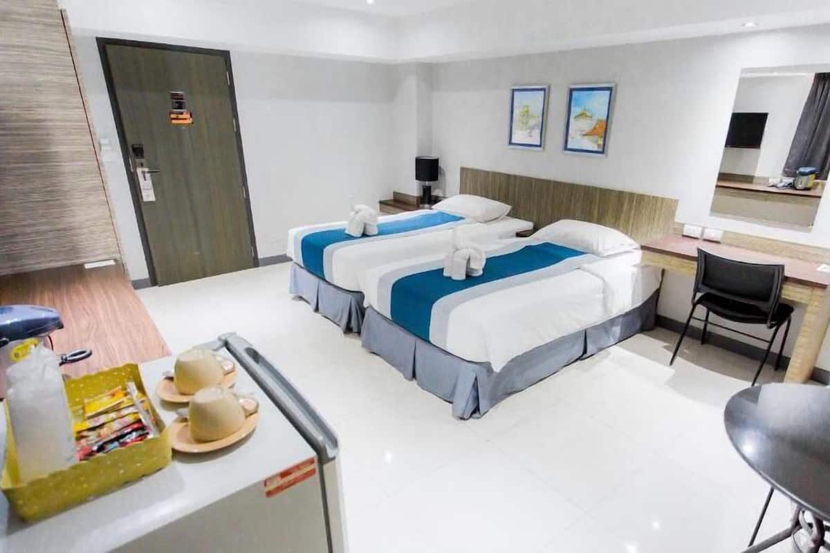 A hotel room with two beds, a desk, a chair, and a small table with a coffee pot and cups.