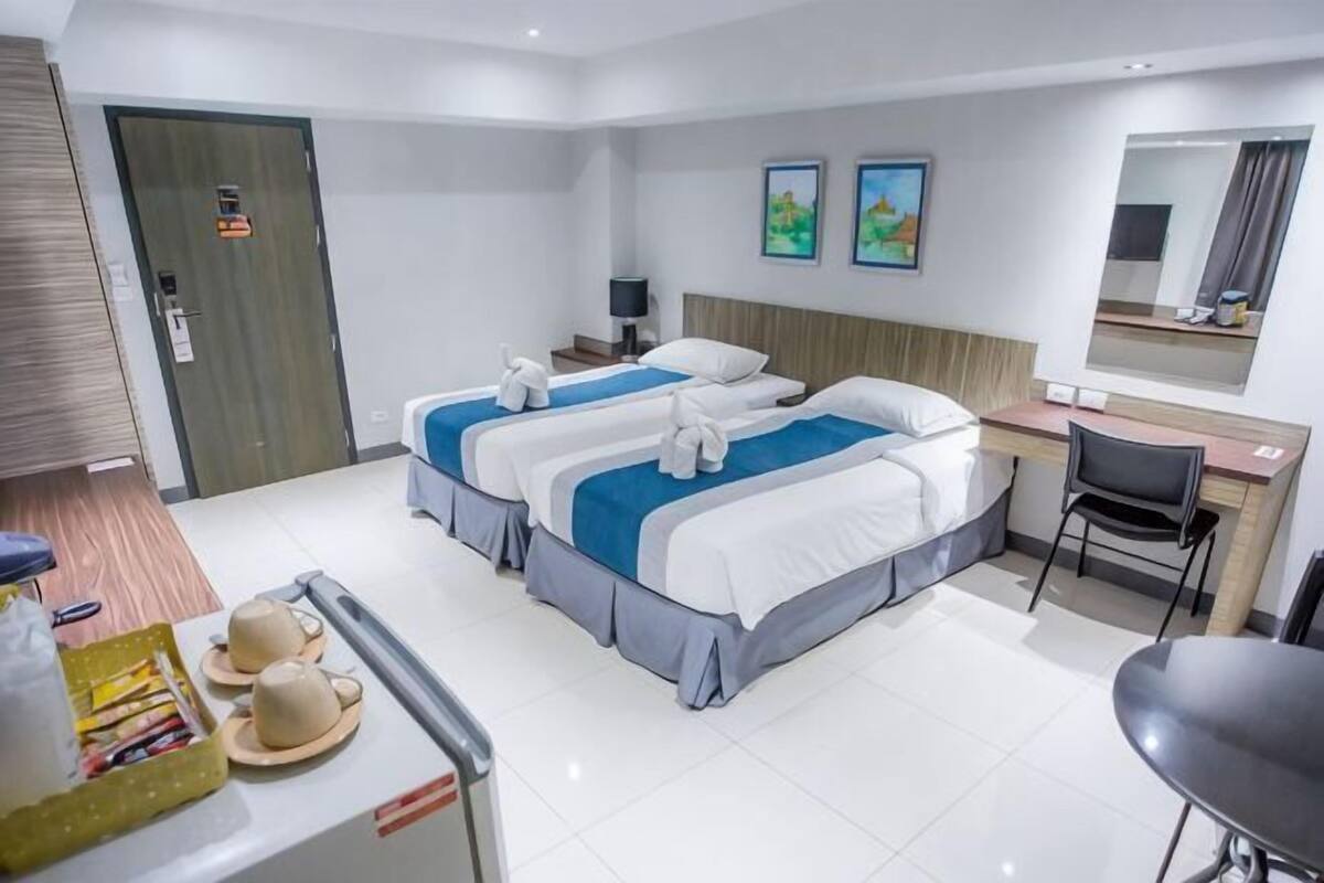 A hotel room with two beds, a desk, a chair, a small table with hats, and a door.