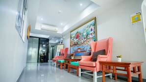 A reception area with a row of pink chairs, a wooden table, and a colorful mural on the wall. - Pho Place (Bangkok)