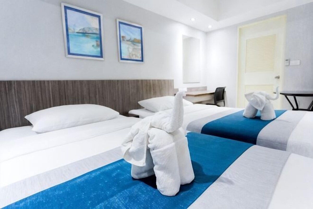 A hotel room with two beds, a desk, and a chair. There are towels on the beds and a door in the background.