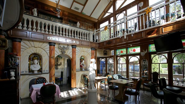 Un intérieur spacieux avec un plafond haut, des colonnes richement décorées et un balcon donnant sur la rue.