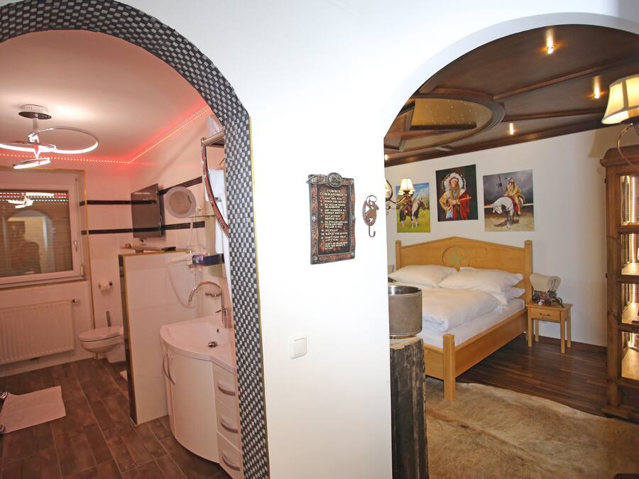 A bedroom with a wooden bed, a nightstand, a lamp, and a wall with framed pictures.