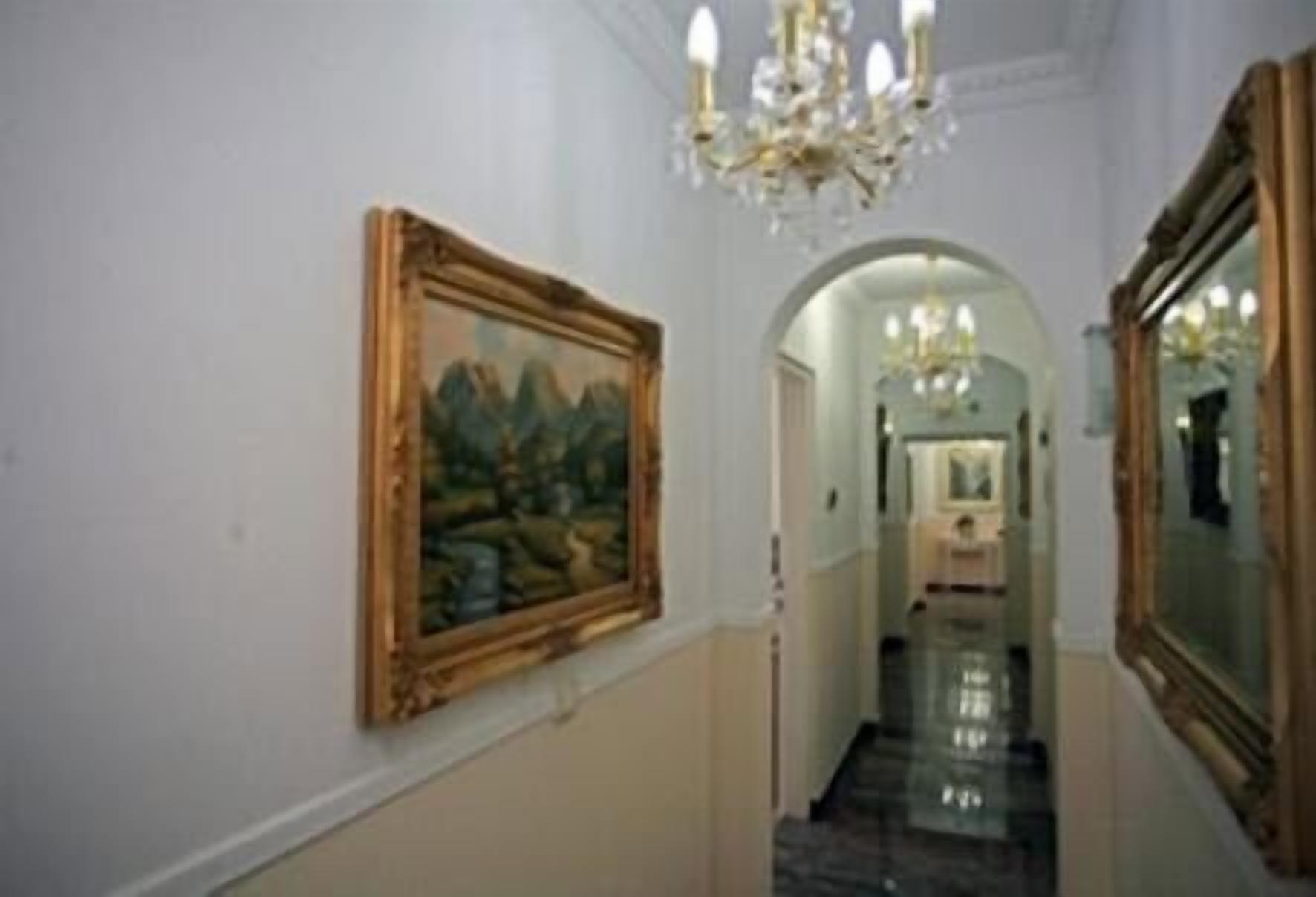 A hallway with a painting on the wall, a chandelier, and a mirror.