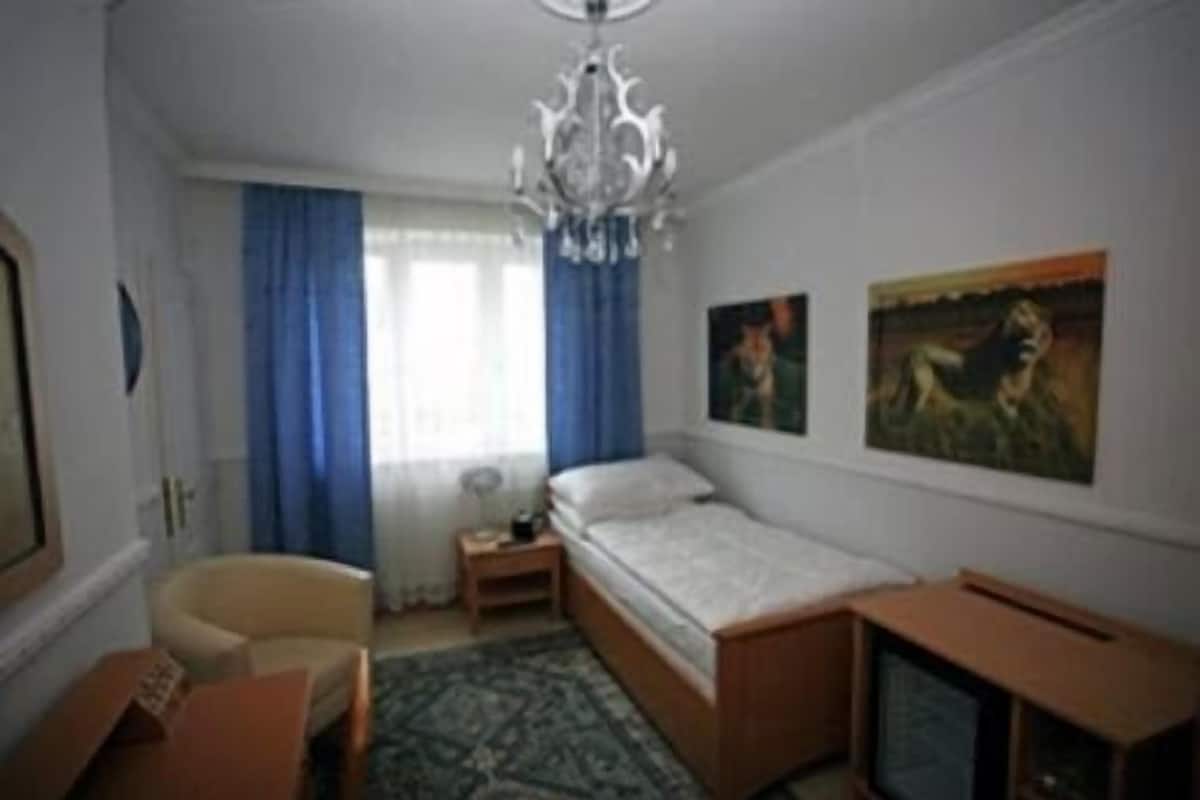 Een slaapkamer met een bed, een stoel, een klein tafeltje, een televisie en twee schilderijen aan de muur.