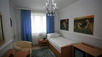 A bedroom with a bed, a chair, a small table, a television, and two paintings on the wall.