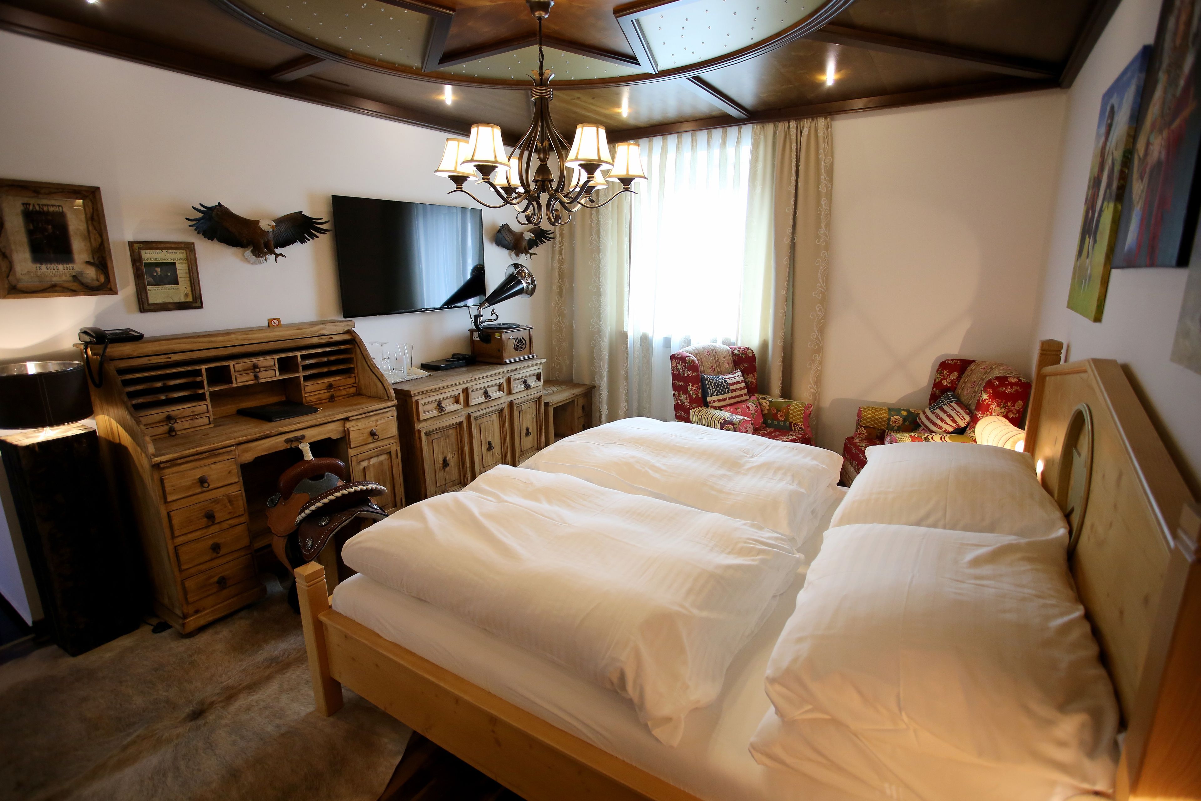 A bedroom with a wooden bed, a desk with drawers, a chair, a television, and a chandelier.