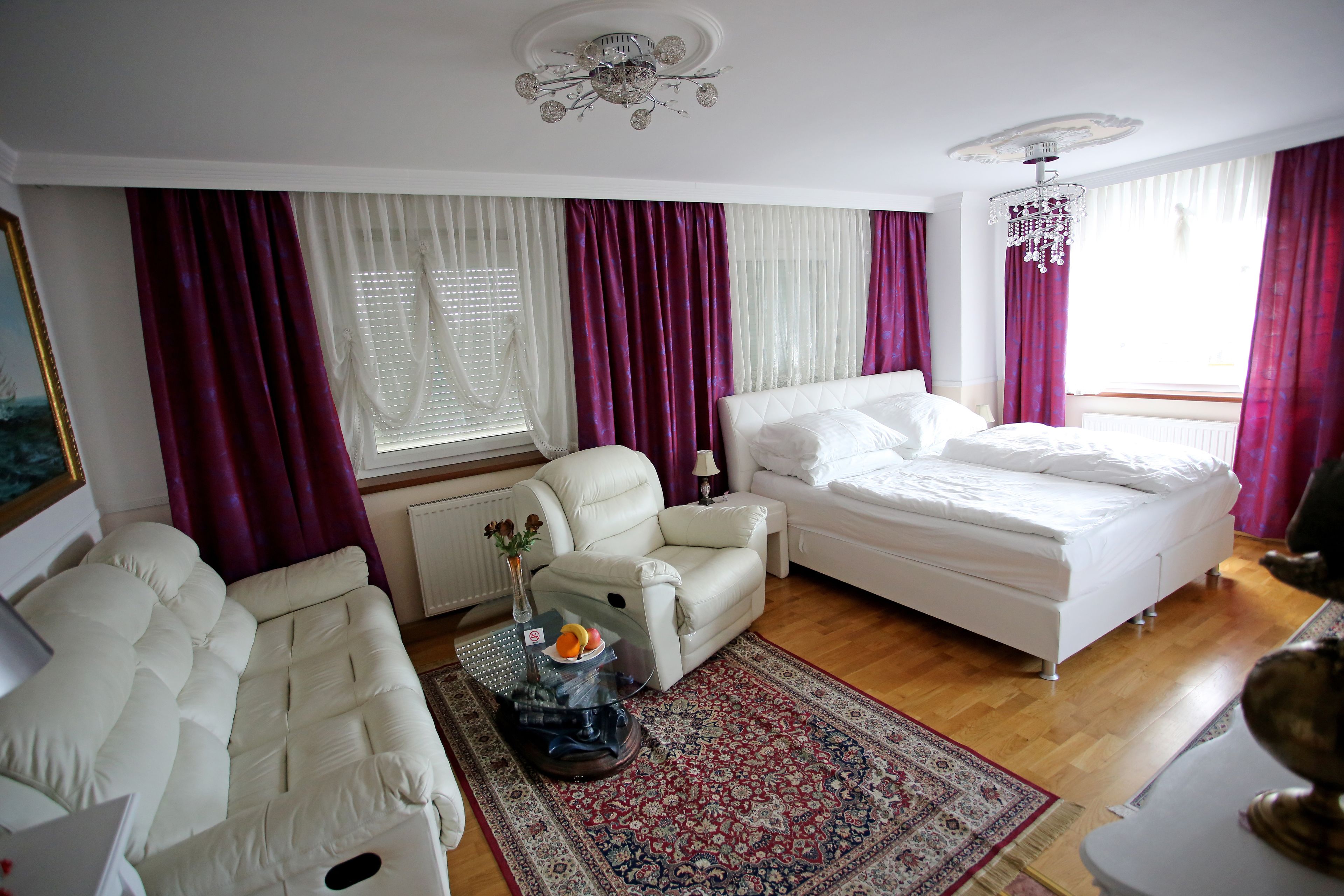 A well-lit bedroom with a large bed, a sofa, and a coffee table with a vase and fruit.