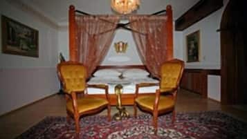 Una stanza con un letto a baldacchino, due poltrone imbottite, un tappeto decorato e un lampadario.