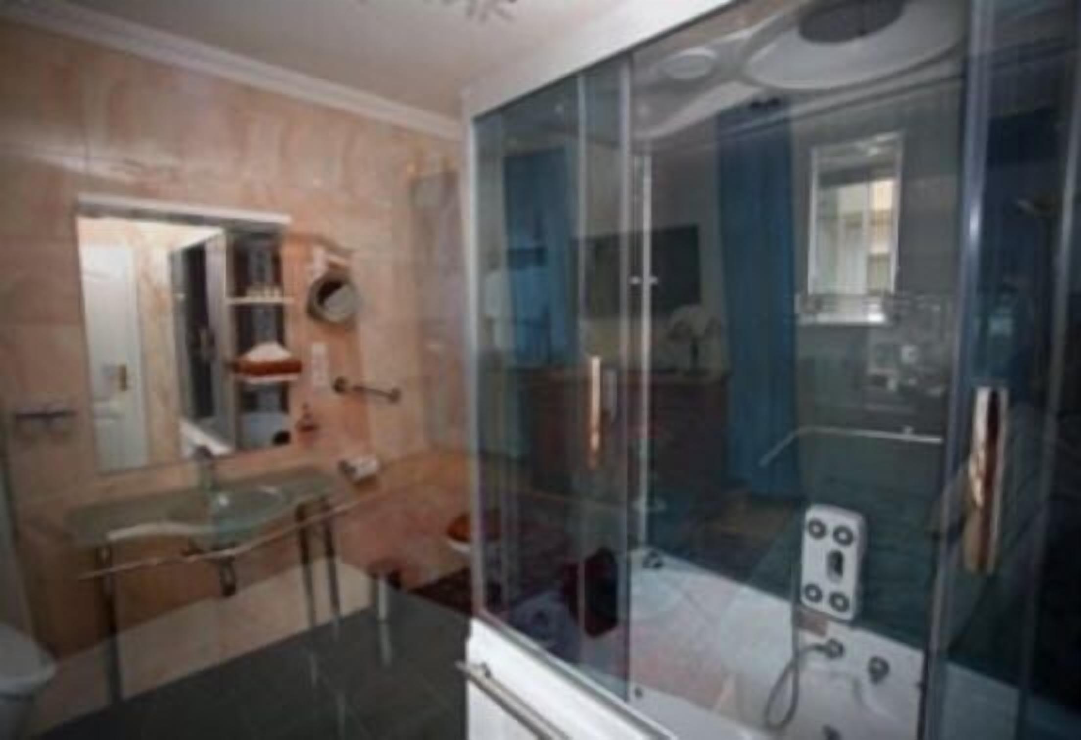 Un baño moderno con cabina de ducha de vidrio, lavamanos de vidrio y pared con azulejos de mármol.