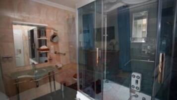 Un baño moderno con cabina de ducha de vidrio, lavamanos de vidrio y pared con azulejos de mármol.