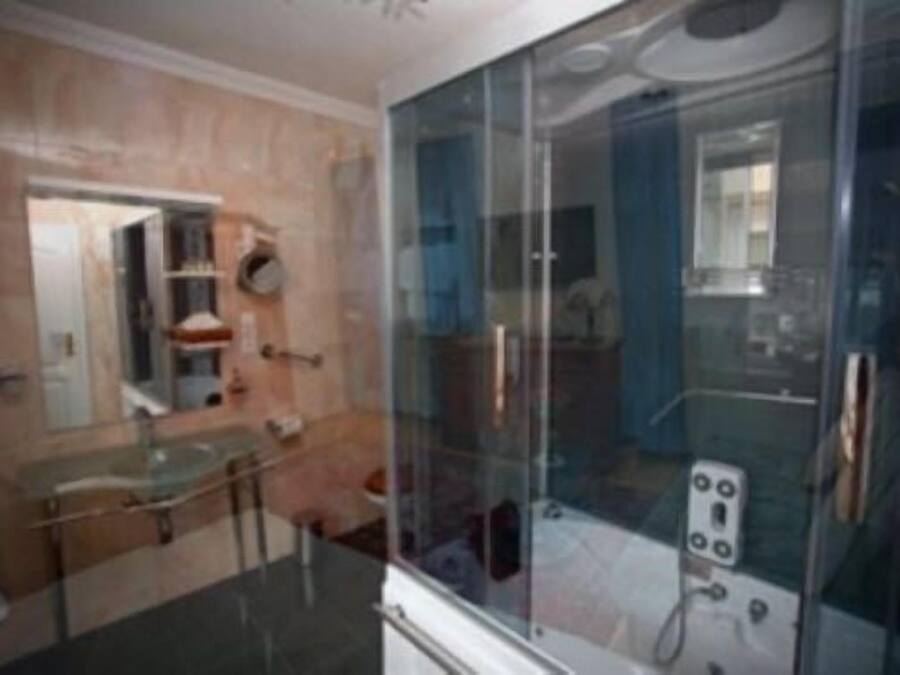 Un baño moderno con cabina de ducha de vidrio, lavamanos de vidrio y pared con azulejos de mármol.
