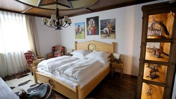 Una cama bien hecha con ropa blanca, cabecera de madera y mesita de noche con lámpara. Hay tres cuadros colgados en la pared que representan figuras históricas.