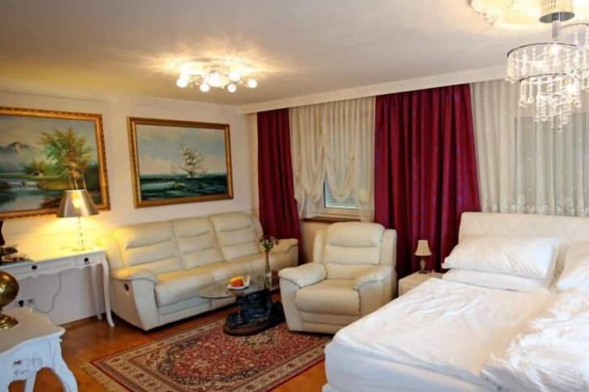 Hotelkamer met een bed, een bank, een stoel, een bureau met een lamp en twee schilderijen aan de muur.