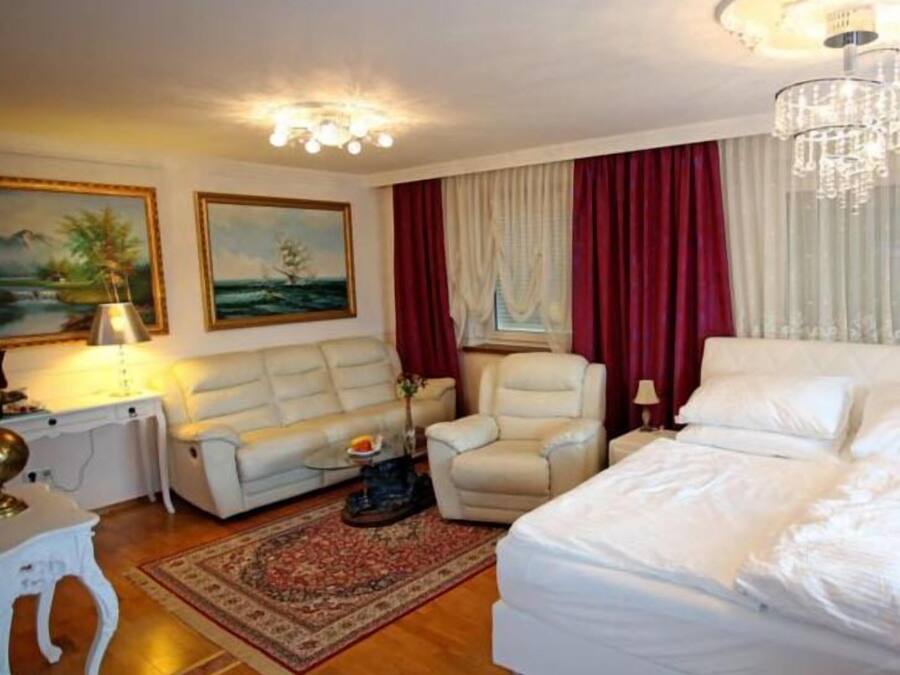 Habitación de hotel con cama, sofá, sillón, escritorio con lámpara y dos cuadros en la pared.