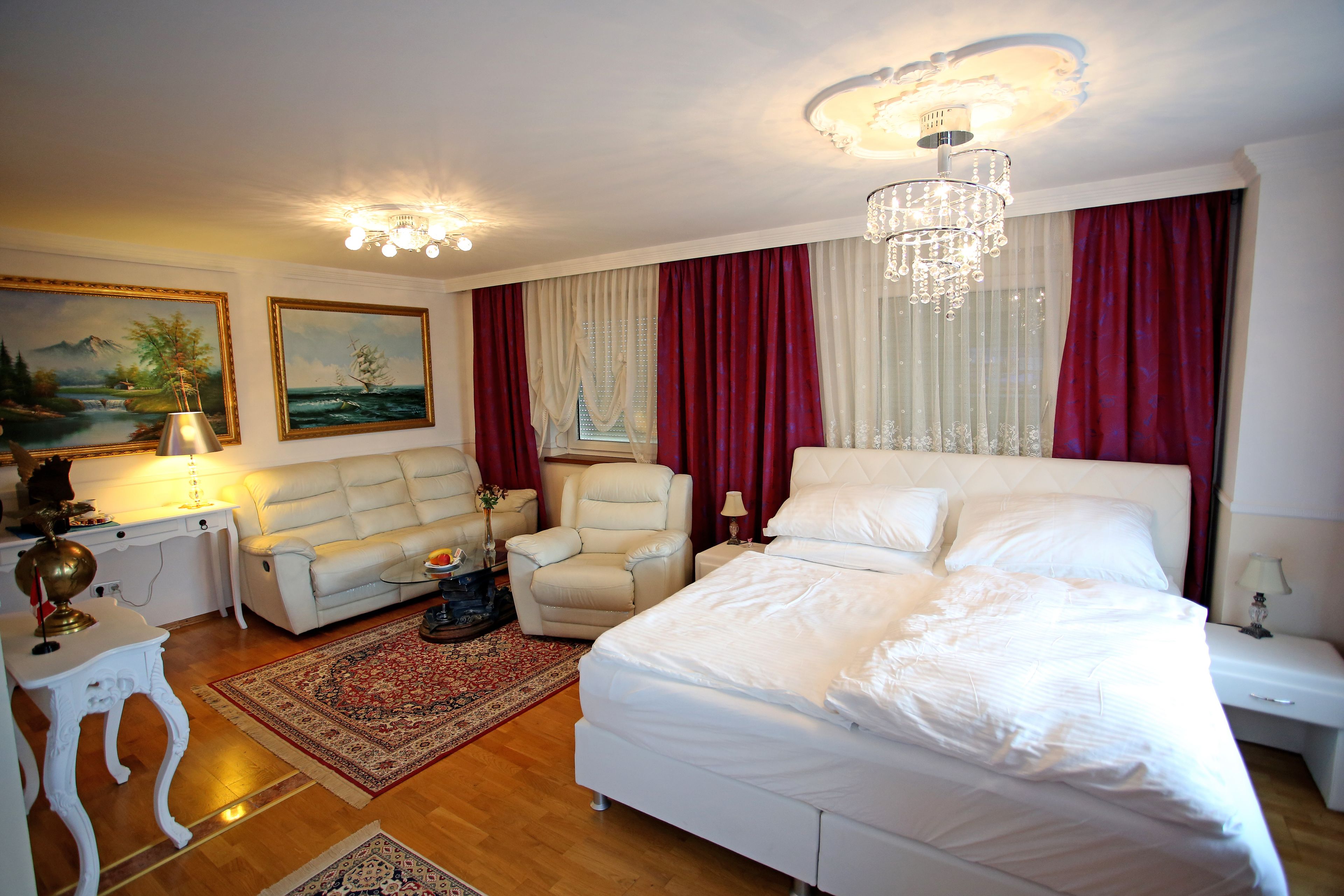 A bedroom with a large bed, a sofa, a chair, and a desk with a lamp.
