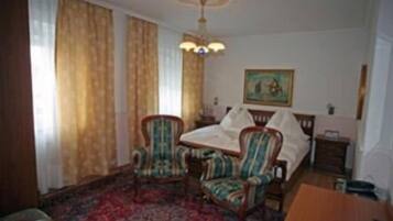 Een hotelkamer met een bed, twee fauteuils, een tafel, een kroonluchter en een schilderij aan de muur.