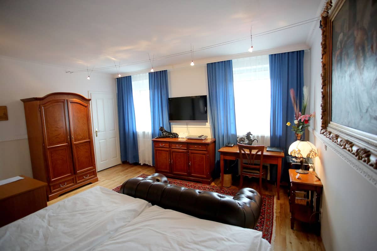 Een slaapkamer met een bed, een houten kledingkast, een bureau met stoel, een televisie en een lamp.