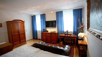 Quarto com cama, guarda-roupa de madeira, escrivaninha com cadeira, televisão e abajur.