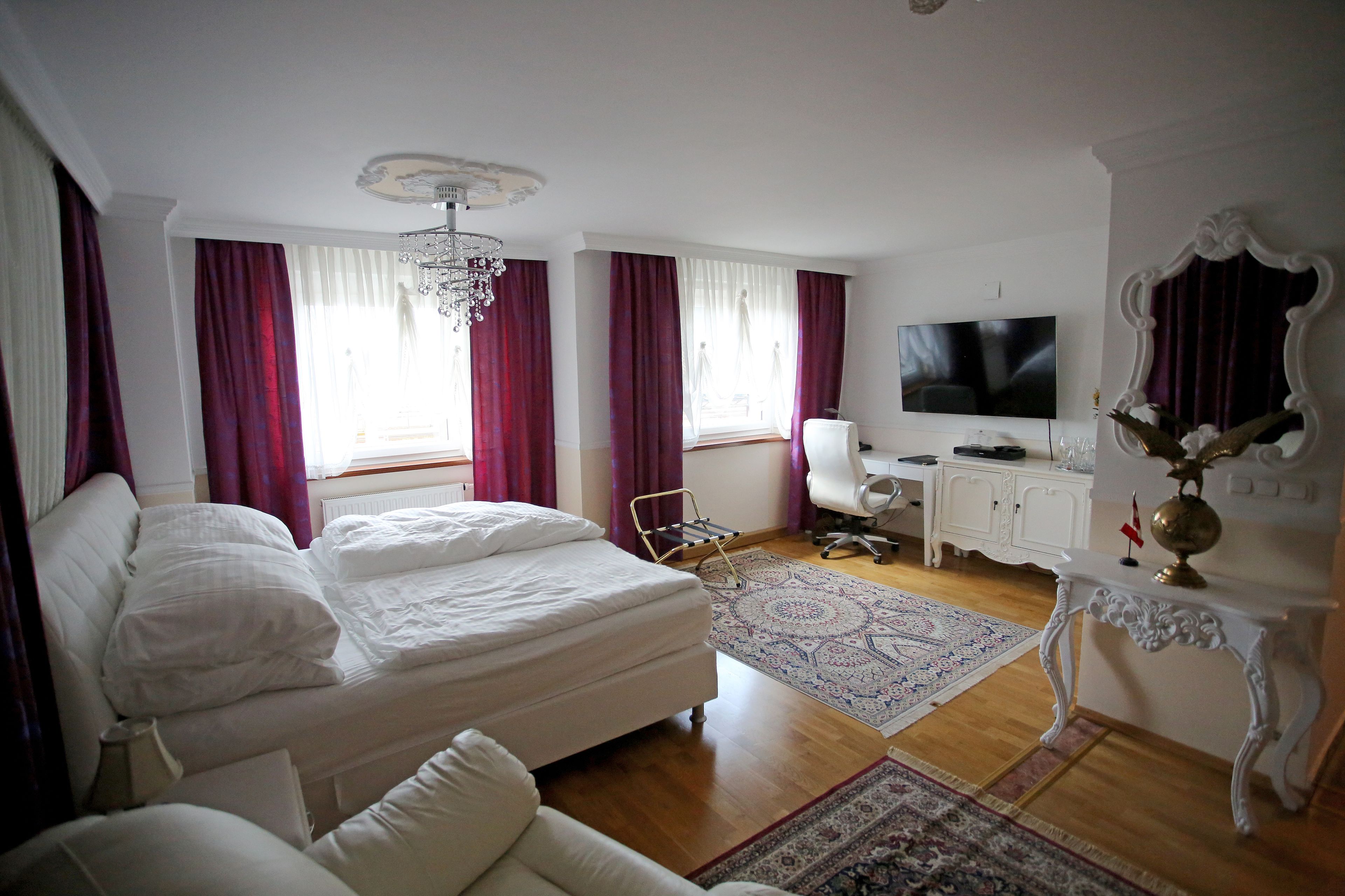 A hotel room with a bed, a desk, a television, and a chandelier.