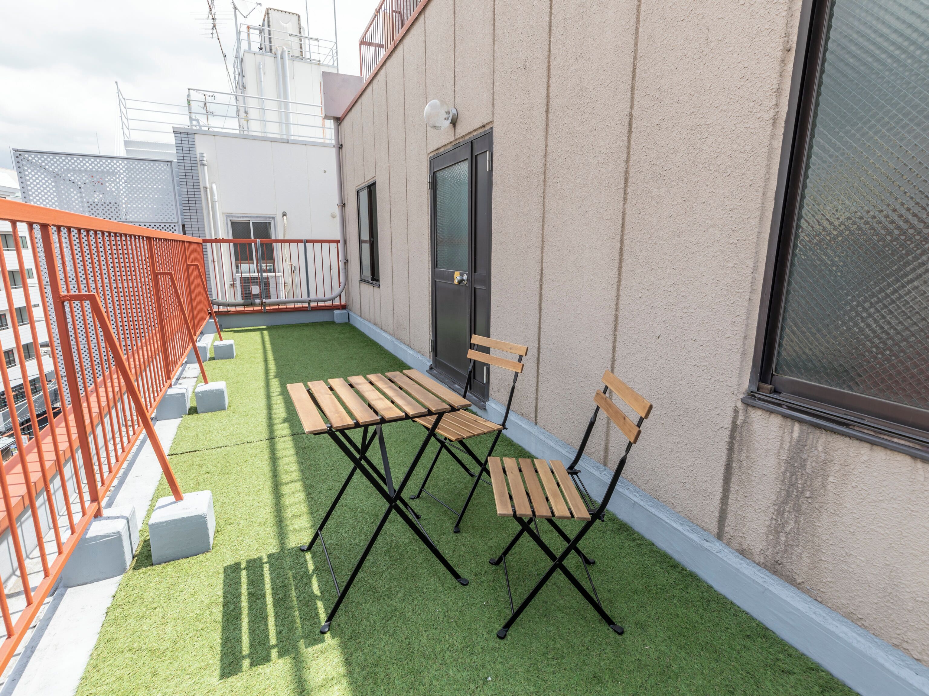 A rooftop terrace with artificial grass, wooden furniture, and a metal railing.