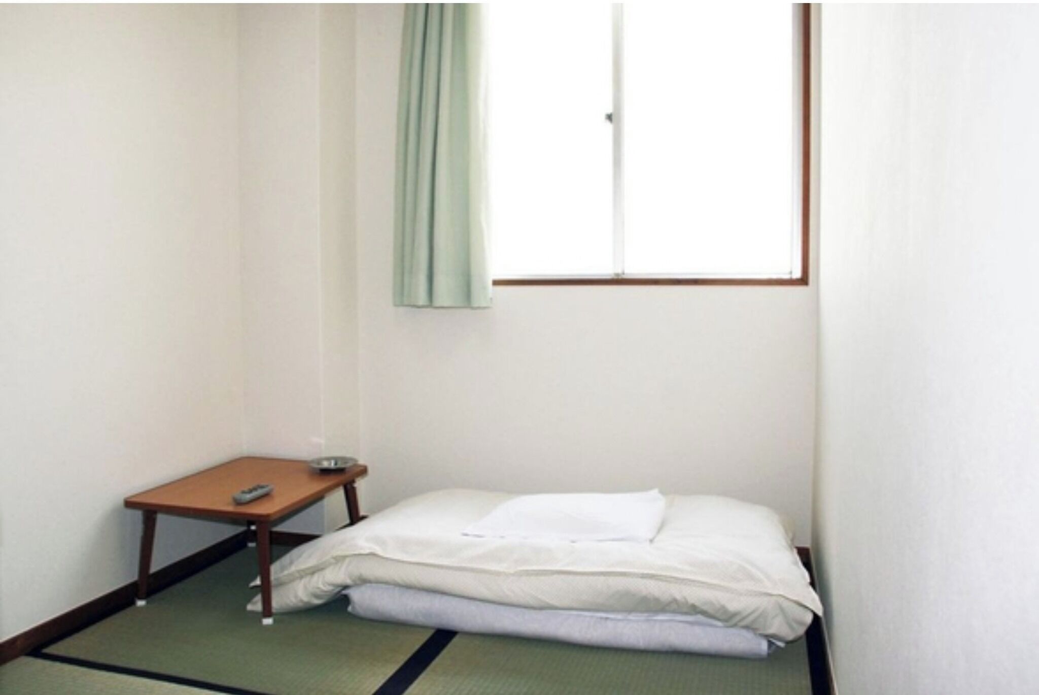 A small, sparsely furnished room with a single bed, a small table, and a window.