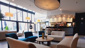 Een moderne lounge met banken en fauteuils, een bar met flessen, en grote ramen die natuurlijk licht binnenlaten.