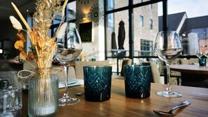 Een eettafel met een vaas gedroogde bloemen, drie wijnglazen en twee blauwe glazen.'