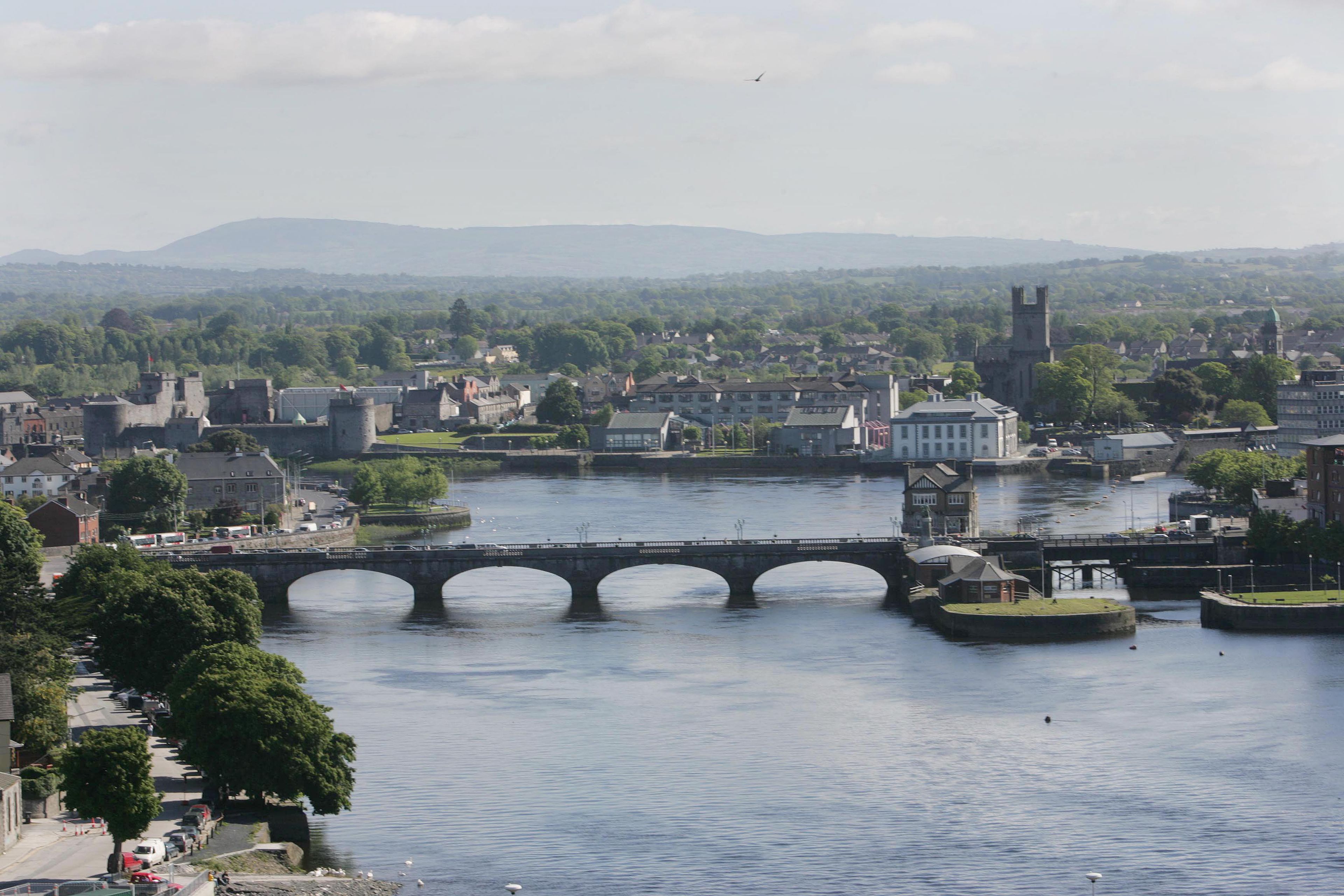 A river with a stone bridge, buildings, and a church with a tower.