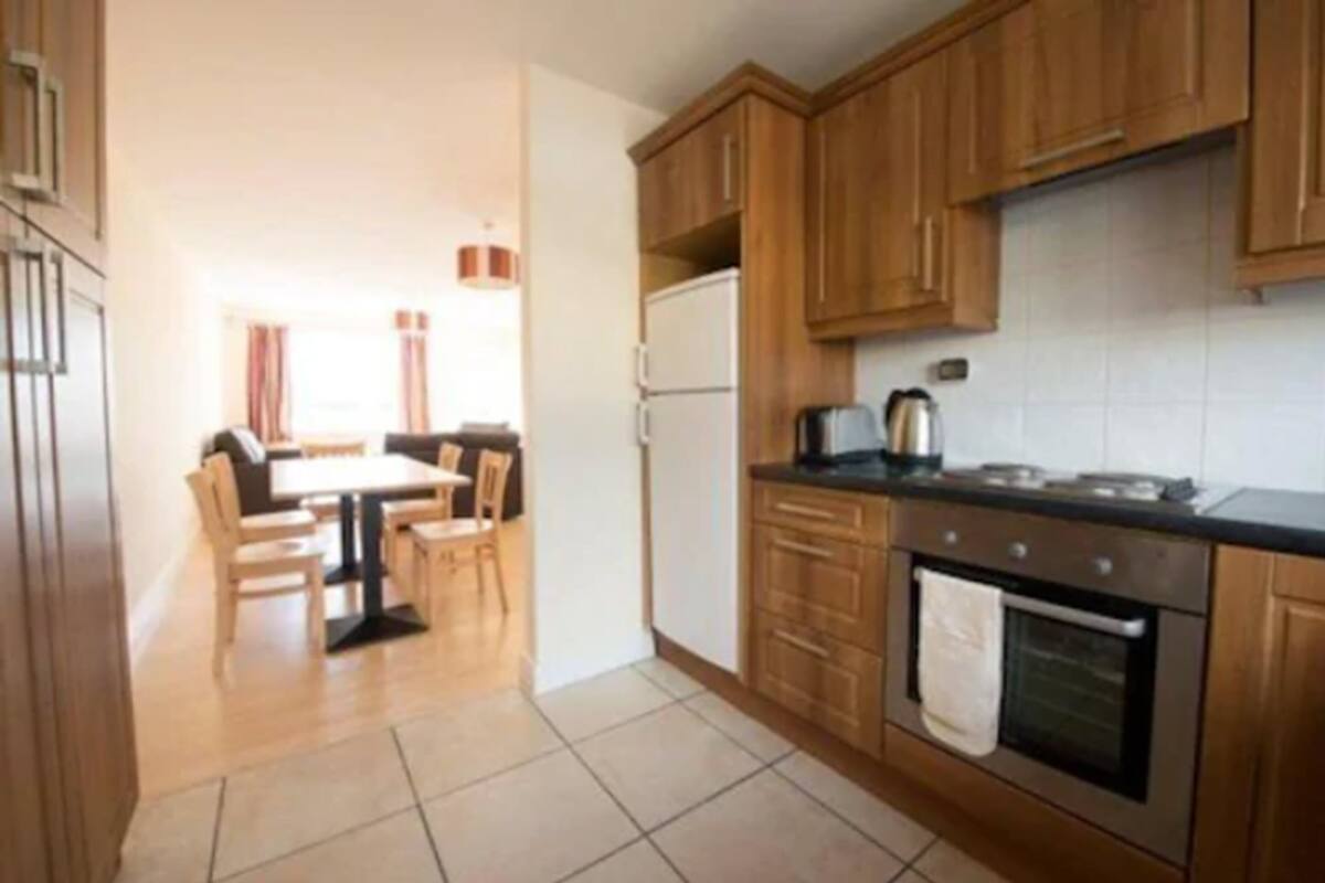 A compact kitchen with wooden cabinets, a refrigerator, a stove, and a dining area with chairs and a table.