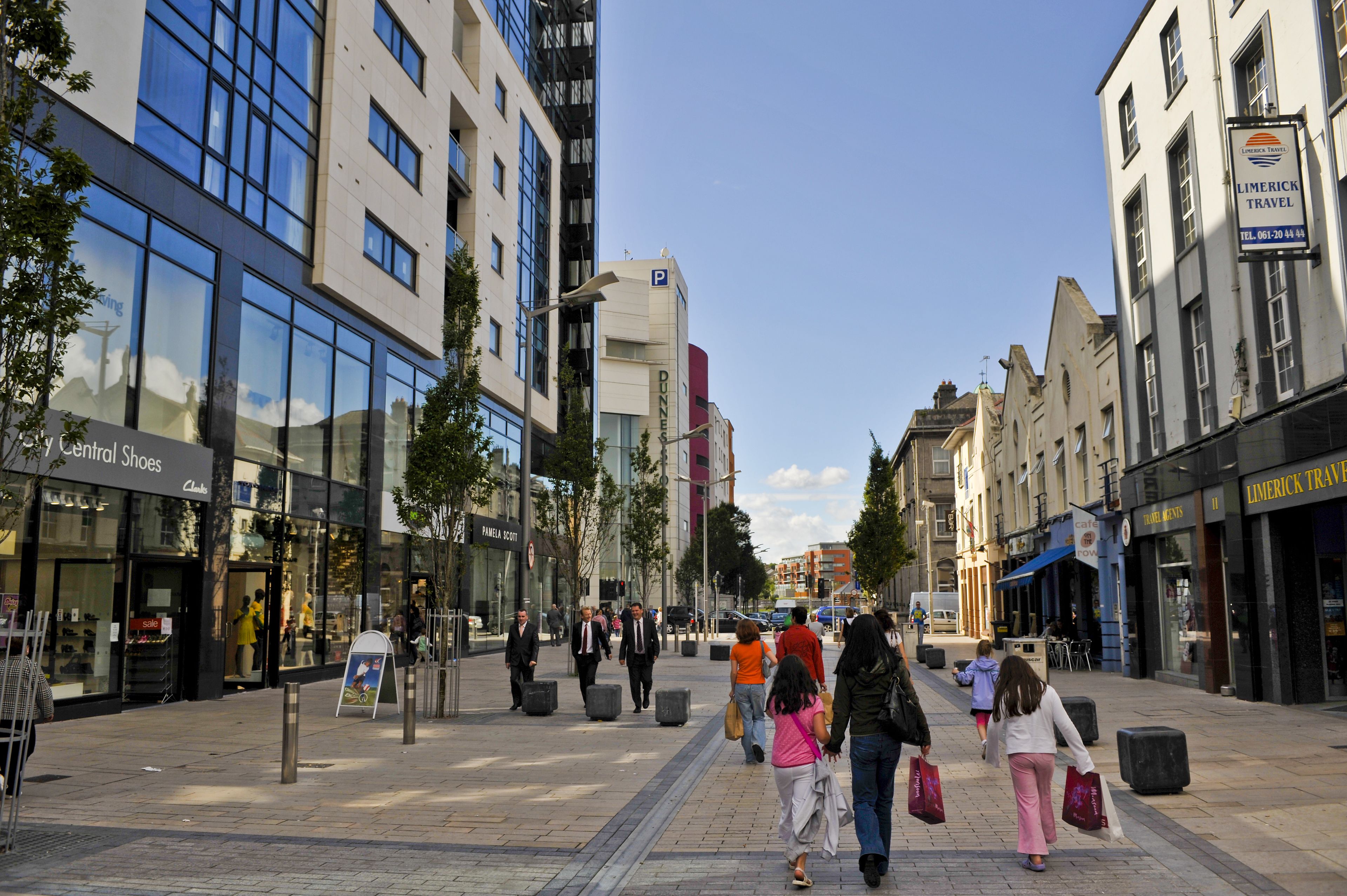 A pedestrian street lined with modern buildings, including a hotel named 'Dunnes'.