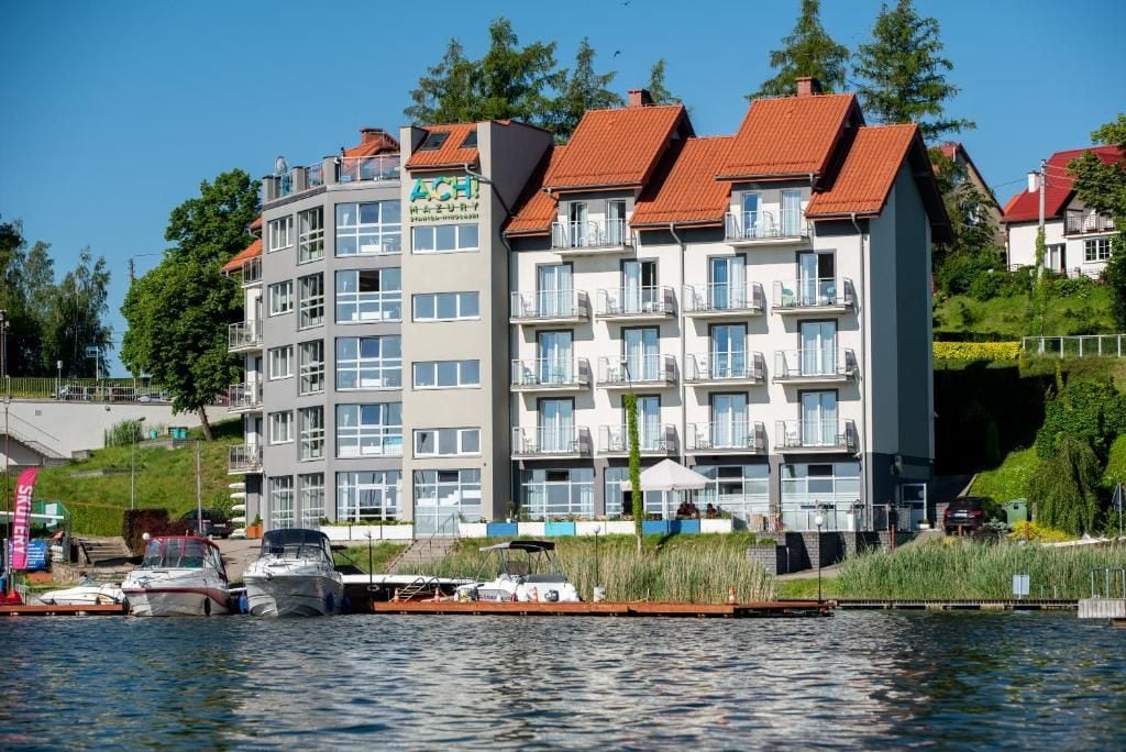 Een meerhoog gebouw met balkons, een steiger met boten en een heldere lucht.